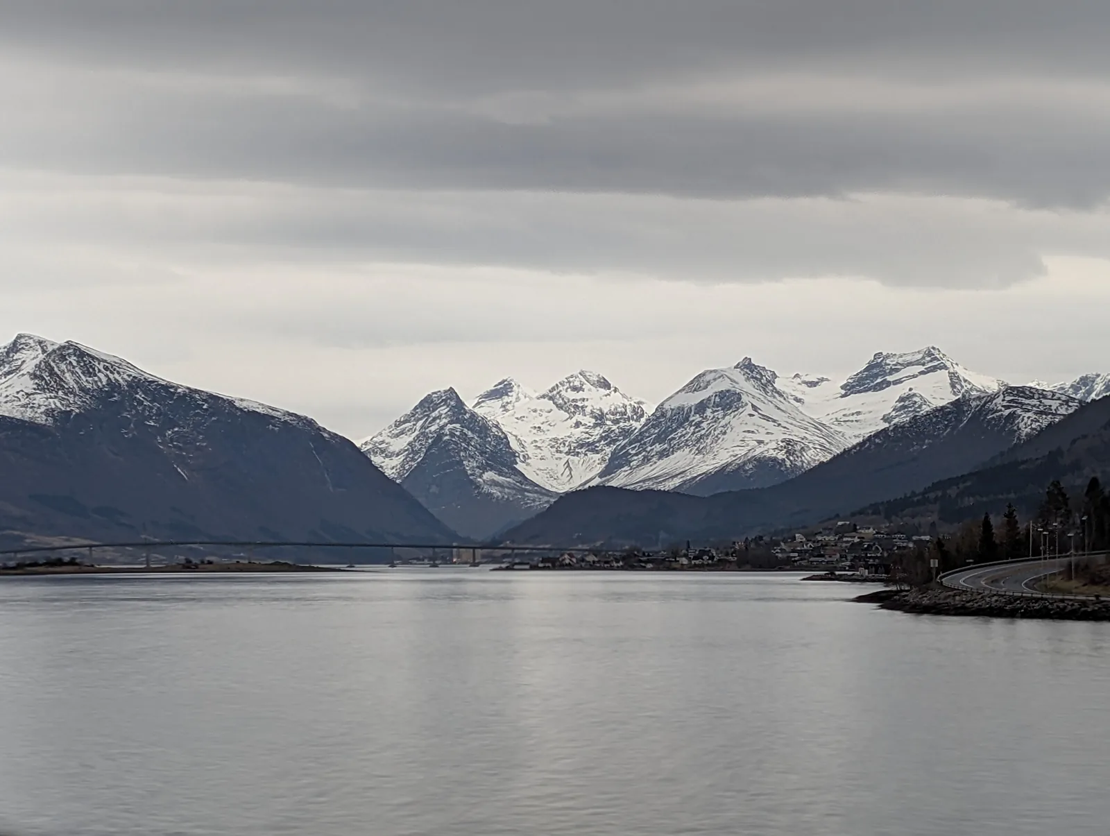 A wide grey fjord lined with snow-covered summits under an overcast sky.