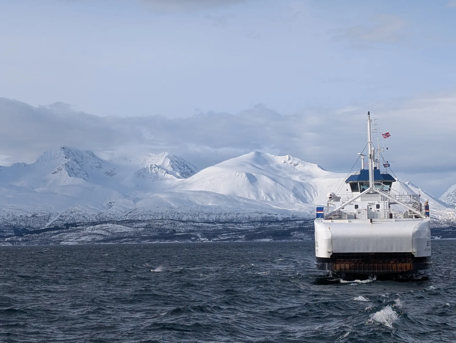 A ferry crossing the fjord in front of the snow-covered wall of the Lyngen Alps.