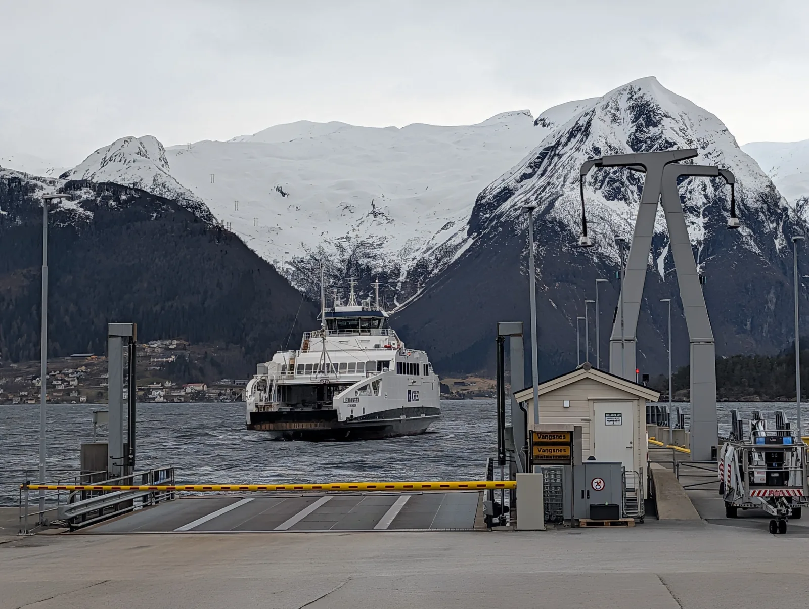 A ferry alongside the quay at the foot of a high snow-covered mountain, the slipway barrier in the foreground.